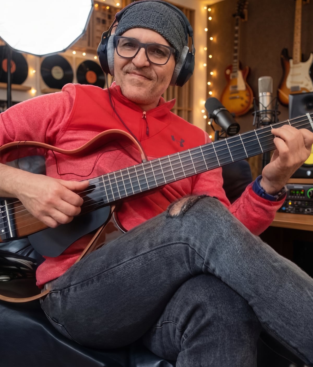 Carlos Rendón in his home studio with headphones and a guitar.